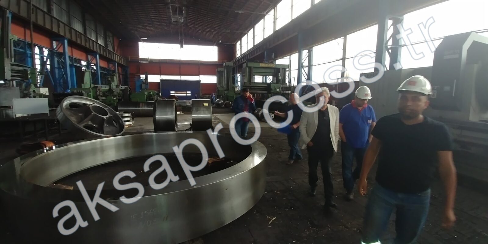 Основатель и команда в цехе тяжелого машиностроения рядом с крупным обработанным помольным кольцом и валками мельницы